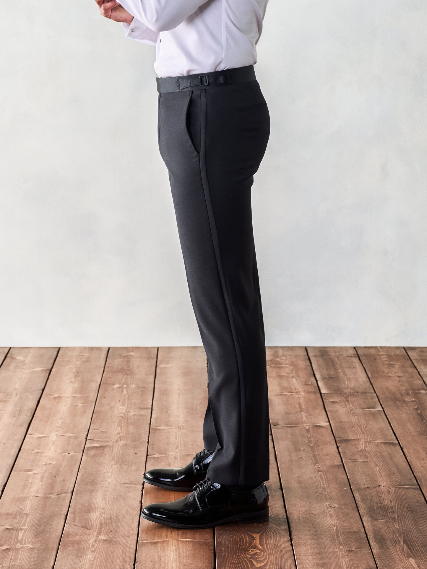 Close-up of the side view of black dress pants, worn by a man standing on wooden floorboards