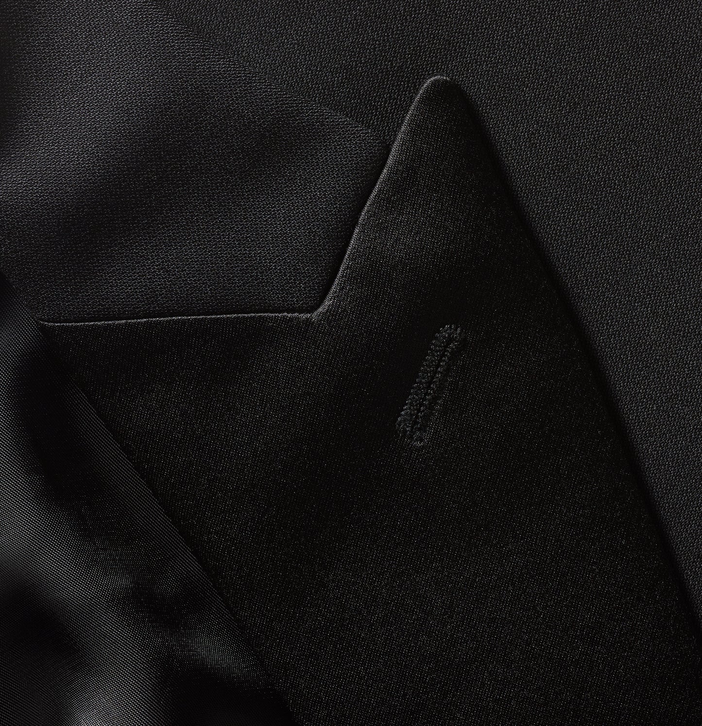 Close-up of a black tuxedo jacket’s peaked lapel and pocket detail.